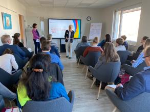 
		Eine Referentin steht vor den sitzenden Zuhörer:innen
	