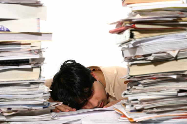 Junger Mann erschöpft zwischen Bücherstapel