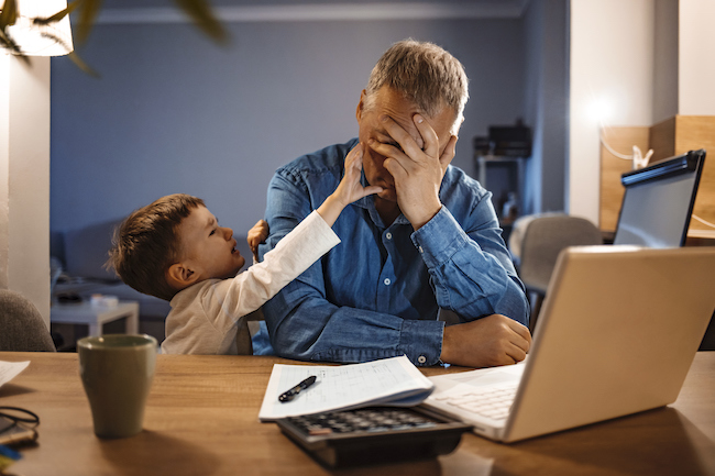 Ein gestresster Vater sitzt am Laptop mit seinem Sohn