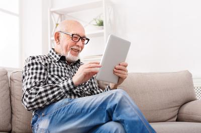 Älterer Mann schaut fröhlich in ein Tablet