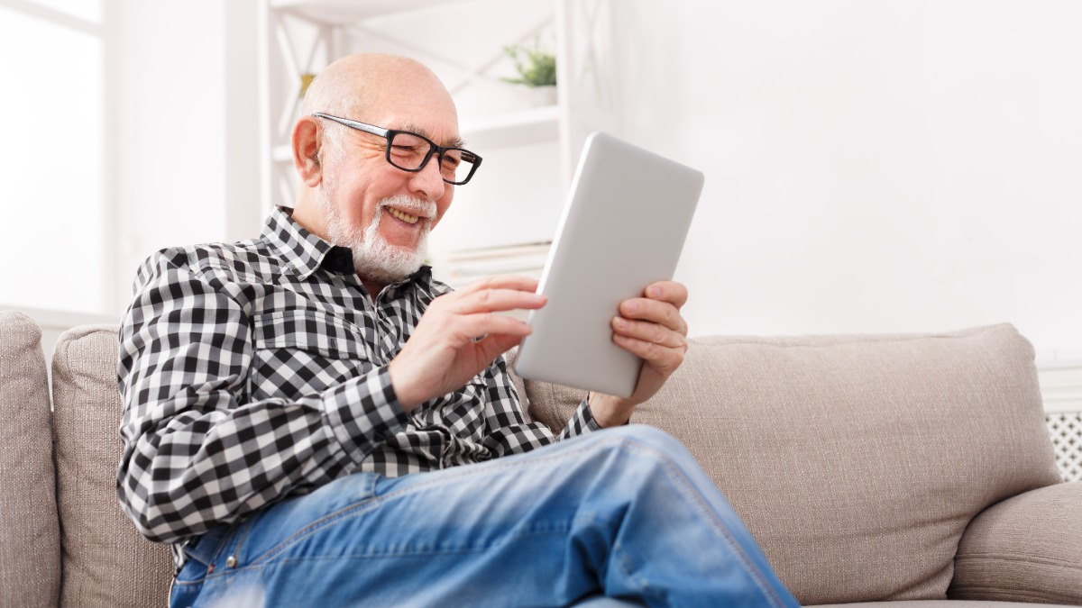 Älterer Mann schaut fröhlich in ein Tablet