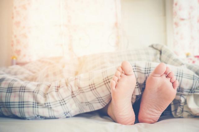 Füße eines schlafenden Menschens ragen aus der Bettdecke hervor