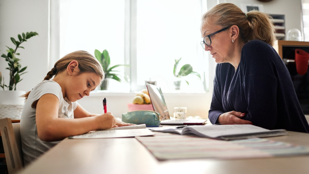 Mutter sitzt mit Kind am Tisch und hilft bei den Hausaufgaben