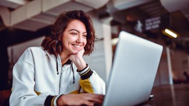 
		Eine junge Frau sitzt lachend vor ihrem Lapop im Büro und ändert ihr Passwort
	