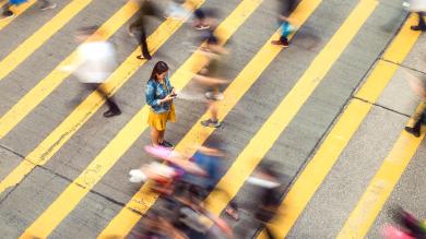 
		Eine Frau läuft auf über einen gelben Zebrastreifen und tippt auf dem Smartphone etwas
	