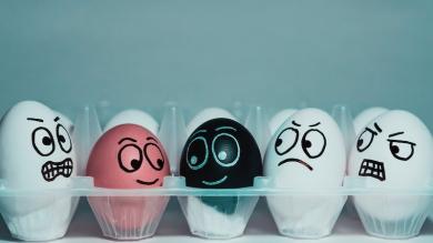 
		2 lächelende farbige Eier sind umgeben von weißen Eiern, die zornig auf die beiden andersfarbigen Eier blicken.
	