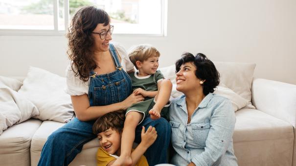 
		Zwei Frauen mit ihre Kindern spielen glücklich zuhause im Wohnzimmer
	