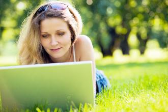 Frau liegt mit einem Laptop in einer Wiese und arbeitet.