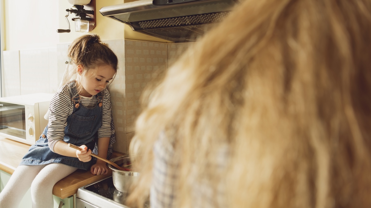 Mädchen sitzt auf Küchentresen und kocht mit der Mutter