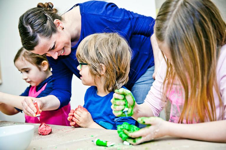 Kinder kneten vergnügt zusammen mit einer Erzieherin